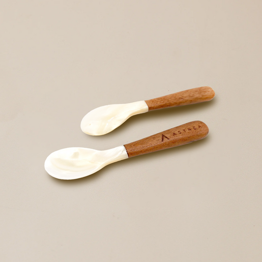 two white caviar serving spoons with wooden handles that say astrea