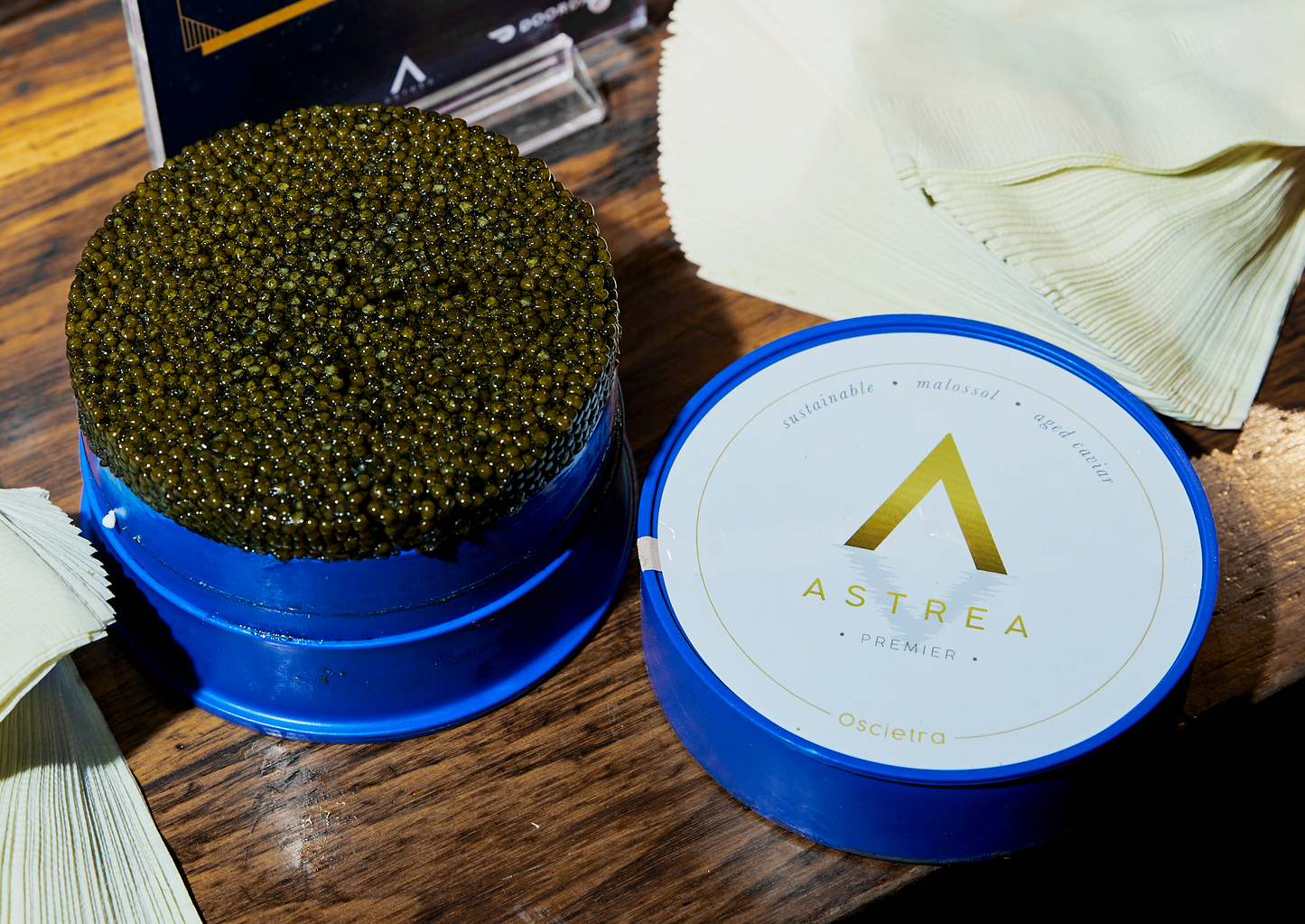 a blue tin of Astrea premier caviar sits on a wooden table