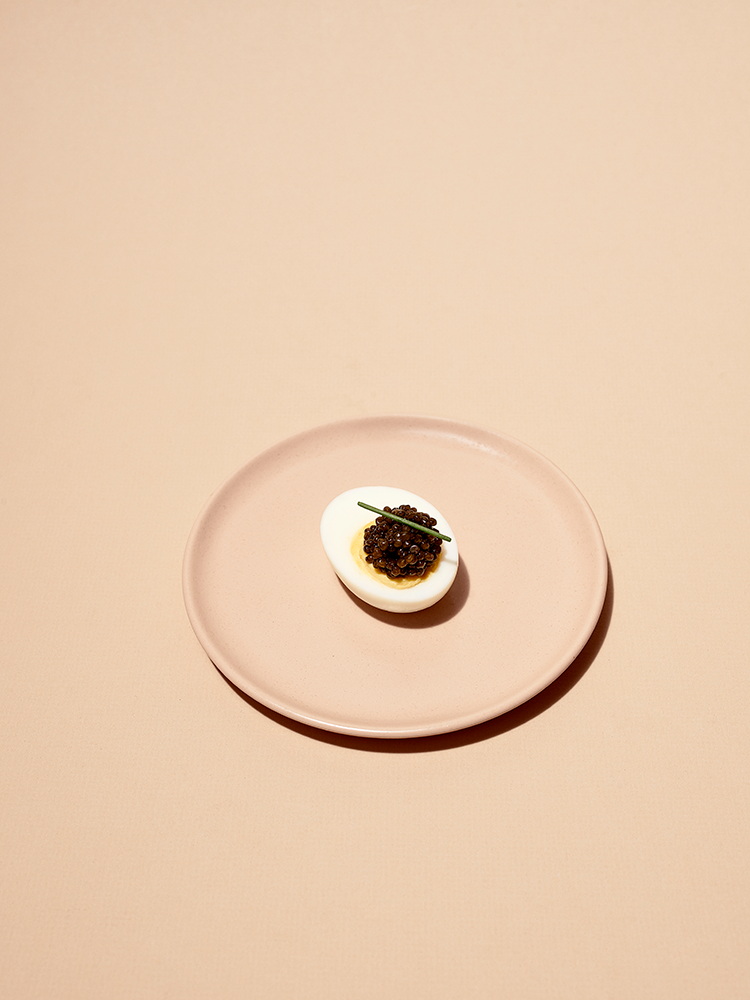 a pink plate with a hard boiled egg and caviar on it